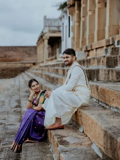 A candid moment of conversation and smiles as the couple sits on the stone steps of a temple tank, their traditional attire adding to the cultural richness of the scene.