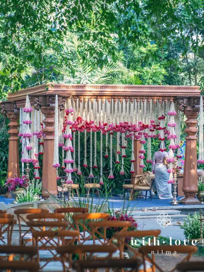 A view of the summer wedding mandap through the guest seating, showing the beautiful layers of flowers and foliage.