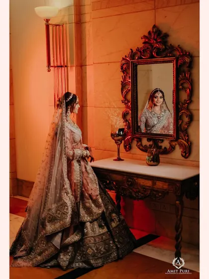 A regal bridal portrait, with the bride looking at her reflection in an ornate mirror. This classic pose and the warm lighting create a timeless and elegant image.