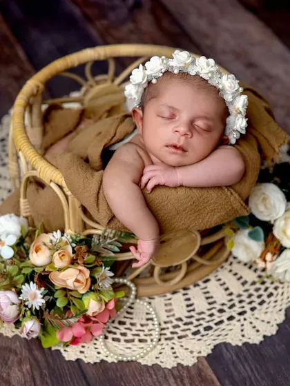 A baby rests comfortably in a small rattan chair, surrounded by flowers. We use various props to add texture and interest to our photos.