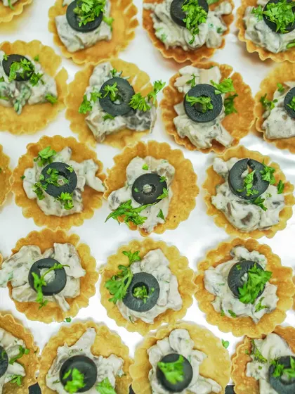 A top-down view of my creamy mushroom tarts, garnished with fresh parsley and black olives. I prepare these in large batches for events of any size.