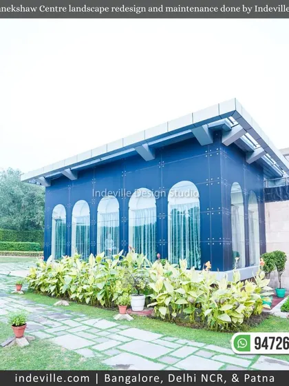 A glass-walled building at Manekshaw Centre, surrounded by neat lawns and planters, showcasing the integration of modern architecture and landscape design.