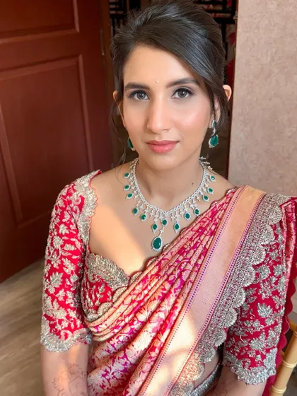 A classic reception look in a beautiful red and pink saree. The makeup is soft and elegant, with an updo that highlights the intricate blouse.