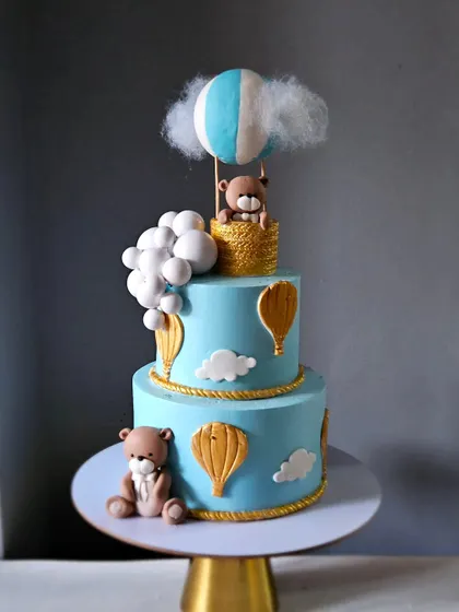 A beautiful blue hot air balloon cake for a first birthday. This two-tiered fondant cake features cute teddy bears and golden rope details for a polished and charming look.