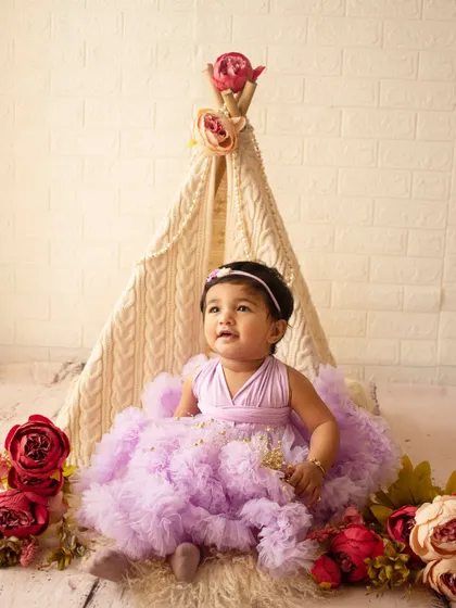 A dreamy first birthday setup with a lace teepee and floral decorations for a beautiful baby girl in a lavender dress.