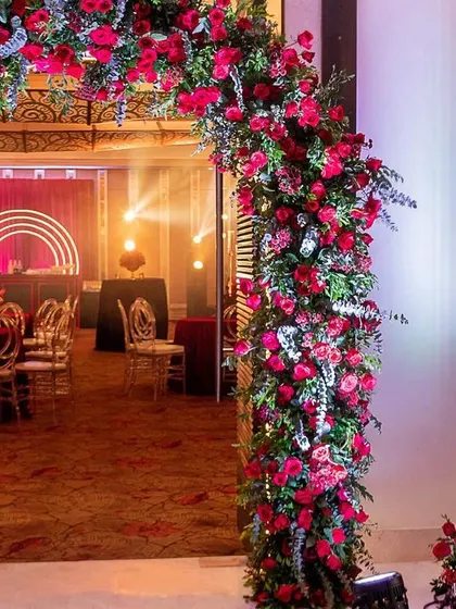 A bold and luxurious reception with a red and black color scheme. The decor includes rich red roses, modern crystal candelabras, and a stylish bar with a neon arch backdrop.