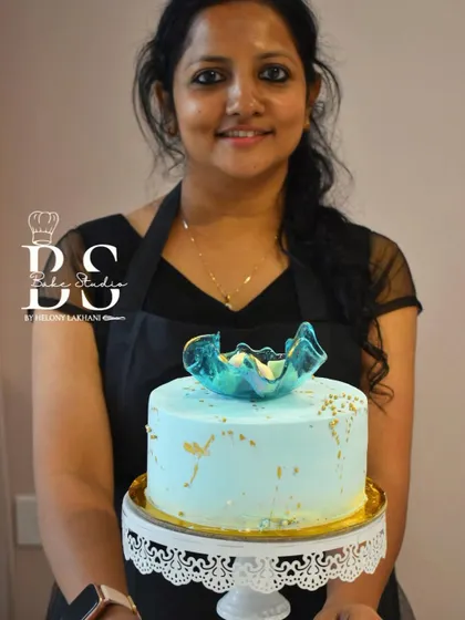 A student holding her elegant light blue whipped cream cake, topped with a delicate, hand-pulled isomalt sculpture.