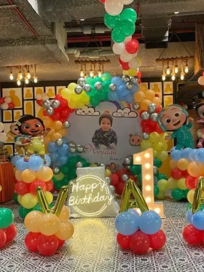 A full view of a Cocomelon-themed first birthday party. This grand setup includes character standees, balloon sculptures spelling the name, and a vibrant backdrop that fills the entire venue.