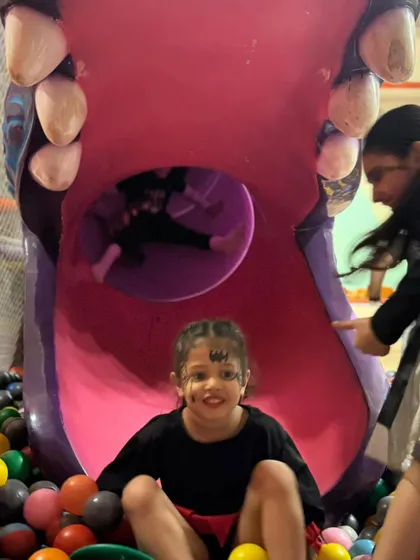 A girl with bat face paint smiles for the camera after her turn on the slide. The play zone is fun for all our spooky guests.