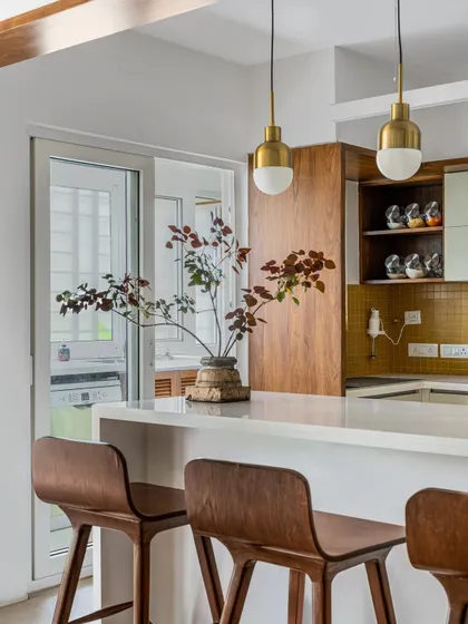 This kitchen from our 'Pepper and Coffee' project features warm wood cabinetry and a mustard yellow backsplash. The breakfast counter with elegant wooden bar stools creates a cozy spot for morning coffee.