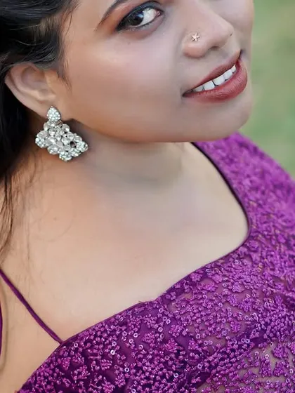 A close-up portrait of a bride in a purple saree, looking over her shoulder with a gentle smile.
