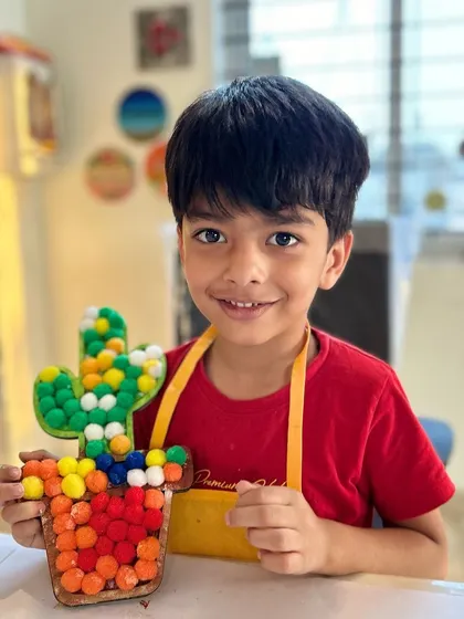A big, happy smile from a young artist who just completed his pom-pom cactus. This activity is all about color, texture, and fun.