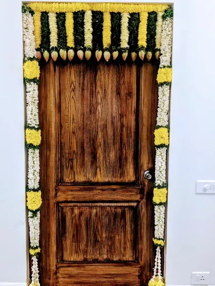 A simple and elegant door frame decoration using garlands of white and yellow flowers. This style is perfect for adding a festive touch to any home ceremony.