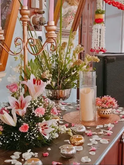 An elegant tabletop arrangement with pink lilies, carnations, and a golden candelabra, creating a romantic and luxurious feel for a wedding reception.