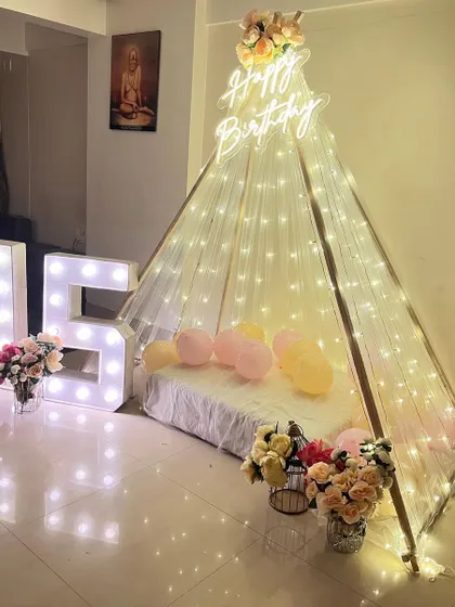 A cozy and dreamy 'Sweet 16' celebration. We set up an elegant teepee canopy draped with fairy lights, paired with light-up marquee numbers and beautiful flower arrangements for an intimate and memorable birthday surprise at home.