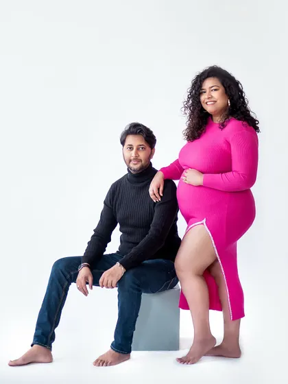 A modern and minimalist studio portrait. The clean white background and bold pink dress create a striking contrast, focusing all the attention on the beautiful mom-to-be.