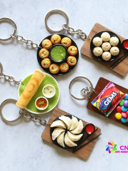 A collection of food keychains, including pani puri, dosa, momos, and Gems.