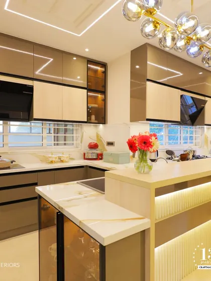 This modern kitchen combines sleek, dual-tone cabinets with a stylish breakfast bar. The design includes a built-in oven and a chimney, with under-cabinet and pendant lighting creating a bright and functional cooking space.