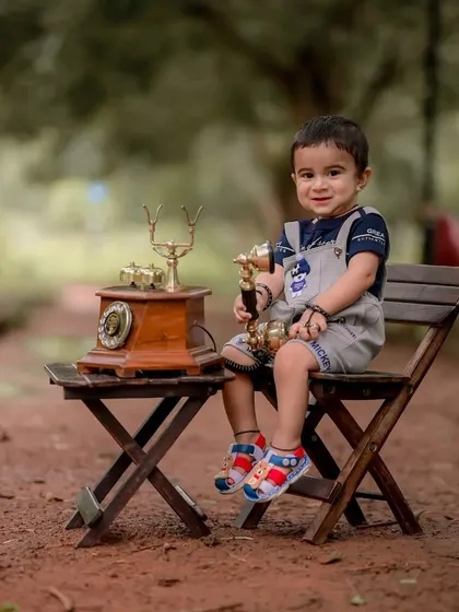 A proud, happy smile from baby Ishan during his vintage-themed photoshoot. The soft, blurred background keeps the focus entirely on his charming expression and the classic telephone prop.