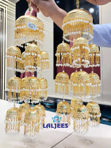 This pair of golden kaleeras features intricate net-work domes and dangling pearl chains, offering a classic and regal look.