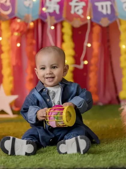 A cheerful baby in a denim jacket enjoys the Diwali setup, complete with lanterns and floral decorations. This shows how modern outfits can also work with festive themes.