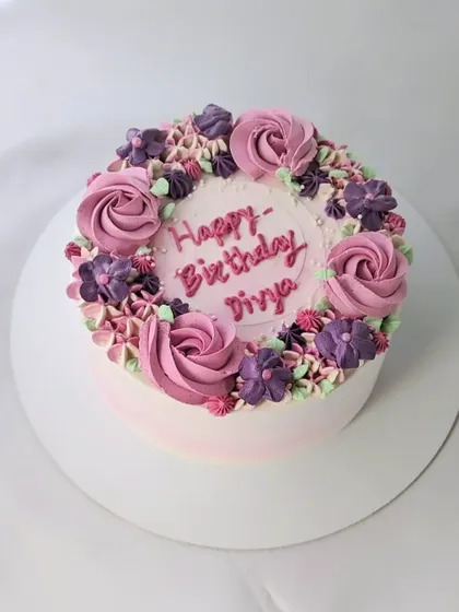 Spring is in the air with this floral cake. The design features a wreath of piped buttercream flowers in shades of pink and purple.