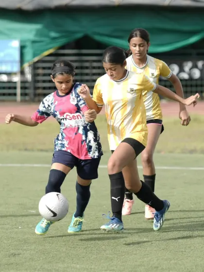 An OriGen player skillfully maneuvers the ball under pressure from two opponents during a competitive match.