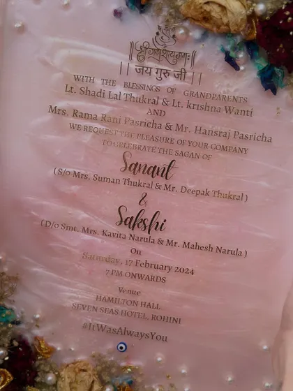 A close-up of a preserved wedding invitation with a beautiful pearlescent pink background. The flowers from the wedding are used to create a delicate border, making the invitation a true work of art.