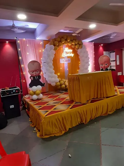 A 'Boss Baby' themed birthday stage. The gold and white balloon arch and character cutouts create a fun and stylish backdrop for the cake cutting ceremony.