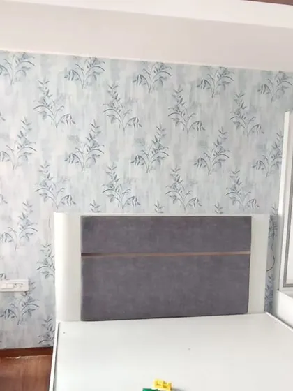 A bedroom accent wall with a blue and white wallpaper featuring a soft, abstract botanical pattern. It creates a calm and artistic backdrop for the bed.