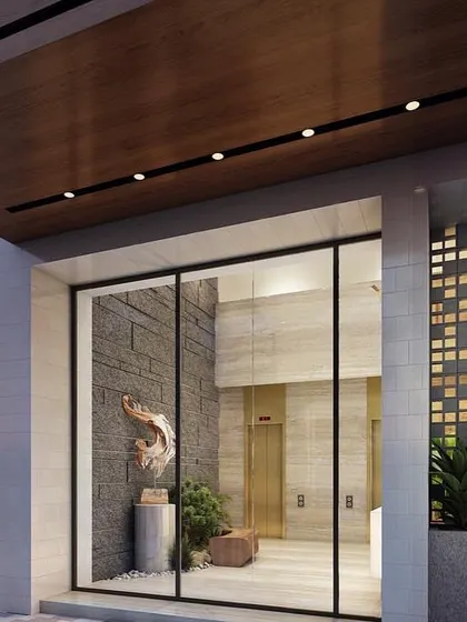 The entrance to the Skylight boutique apartment building features a striking composition of materials. A stone-clad wall with an art sculpture serves as a focal point, framed by glass and a warm wood canopy, offering a glimpse into the building's refined aesthetic.