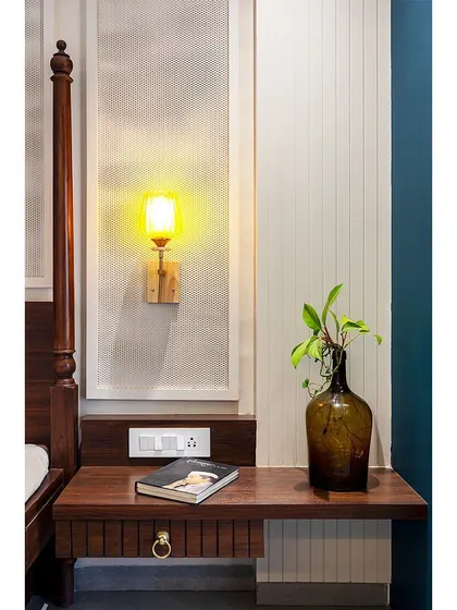 A close-up on the custom bedside table, showcasing the simple, clean design and the warm glow of the vintage-style wall lamp.