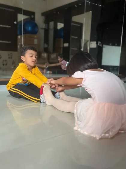A close-up of two young students helping each other with a forward bend stretch.