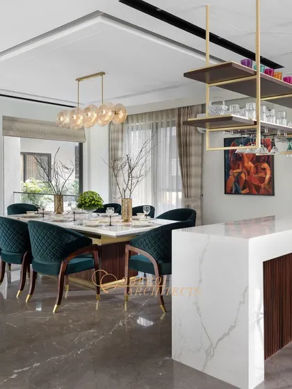 This combined dining and bar area is perfect for entertaining. The design features a marble-topped bar with an overhead rack for glasses and a dining table with plush green velvet chairs.