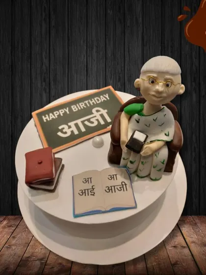 I made this special cake to celebrate an "Aaji" (grandmother). It features a sweet fondant figure of a grandmother teaching, complete with a book and a small blackboard, honoring her wisdom and love.