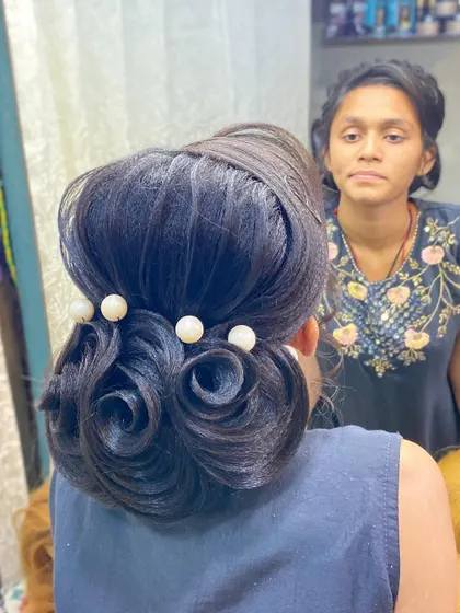 A student's work on a rose bun updo for dark hair, proving that beautiful, detailed styles are possible on any hair color. The pearl accents add a classic touch.