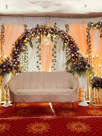 A rustic yet elegant reception stage. This design features a floral arch with orange drapes, complemented by wooden crates and bouquets of flowers, creating a warm and charming look.