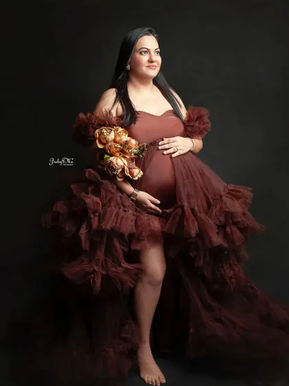 So much glamour in one photo. This mom-to-be looks incredible in a ruffled, high-slit brown gown against a classic dark backdrop, creating a powerful and elegant portrait.