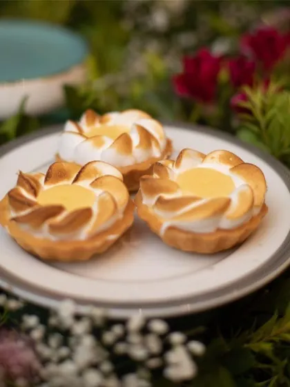 A close-up of our lemon meringue tartlets, nestled in a bed of greenery. The perfectly torched meringue and buttery crust showcase the fine details of our pastry work.