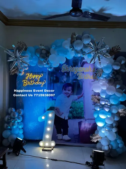 A cool blue and silver theme for a first birthday. This home decor setup includes a personalized photo backdrop, a balloon arch with star-shaped foil balloons, and a light-up number '1'.