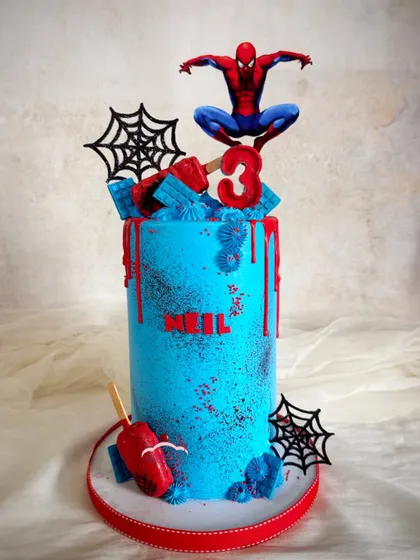 A super tall Spider-Man cake for a 3rd birthday. This design has a dramatic red drip over a bright blue base, complete with spiderwebs and fun cakesicles.
