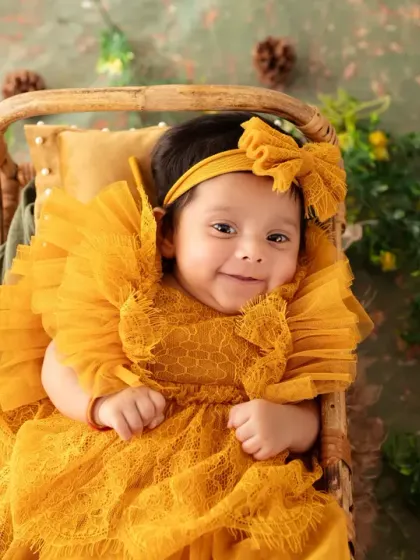 A happy baby girl in a bright yellow dress, smiling brightly during her milestone session.