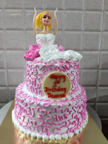 A two-tier doll cake for Deanna's first birthday. The design features a white and pink dress with intricate piping details.