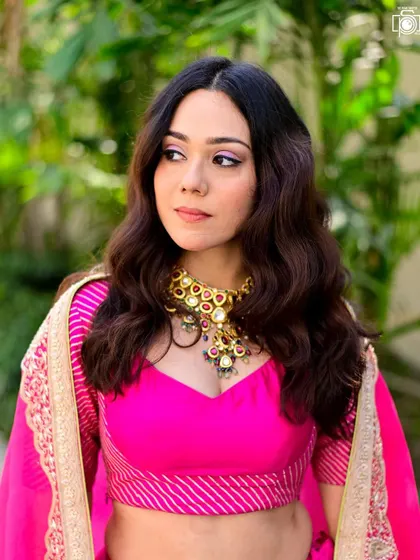 The bright pink lehenga stands out beautifully in this outdoor portrait. The focus is on the model's expression and the stunning traditional necklace, capturing a moment of quiet contemplation.