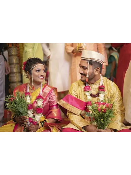 A candid moment of the bride and groom sharing a look during their wedding ceremony. Their yellow and pink outfits are a perfect match for the joyful occasion.