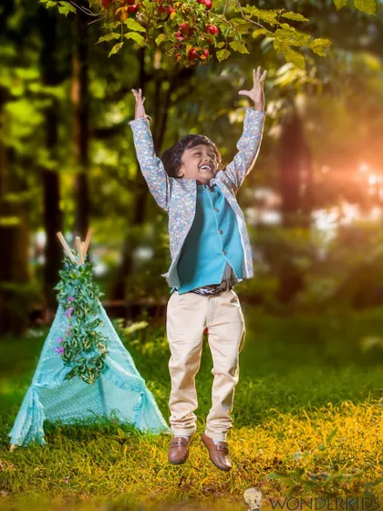 A boy jumps for joy in a green, sunlit park with a teepee in the background. This photo is full of energy and captures the pure freedom of being a kid outdoors.