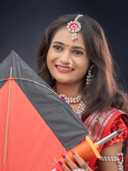 A smiling woman holds a kite and spool of thread, key elements of a Makarsankranti celebration. This studio portrait uses a simple black background to highlight her traditional attire.