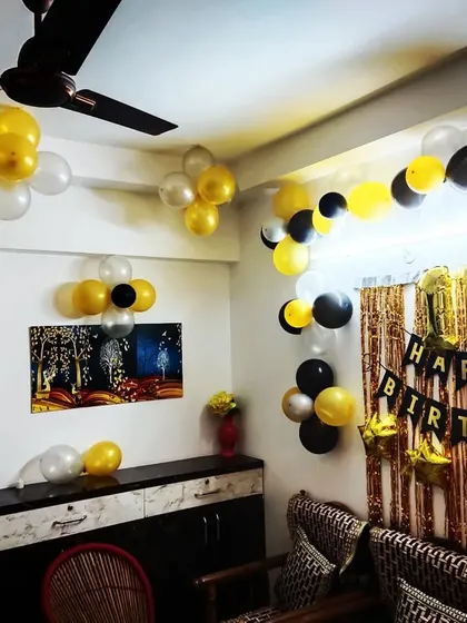 A simple home birthday decoration with black, yellow, and white balloon bunches and a 'Happy Birthday' banner.