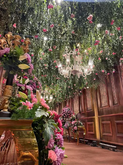 A side view of the entrance passage, showing the sheer density of the floral arrangements. The combination of a lush green ceiling, hanging pink roses, and large floor bouquets created a multi-layered, immersive floral experience.