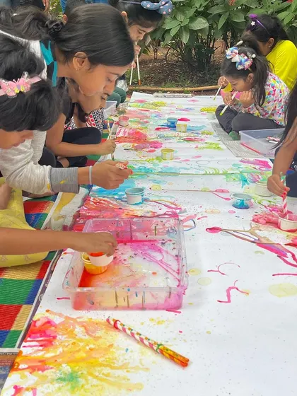 A group of children working together on a long paper scroll, using straws to create bubble art. This is a great example of a collaborative community art project.